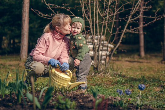 Grandmother with watering can is kissing her cute baby girl in the country. Image with selective focus and toning