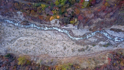 Autumn mountain forest. Top view from a drone. The bright colors of the trees. Green, orange, red, yellow - all colors. A mountain river is visible. There was a mudslide, a strong collapse of the rock