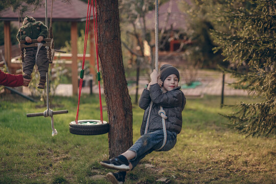 Cute little boy is swinging on a handmade rope swings in the country in Russia. Image with selective focus and toning