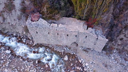 Naklejka premium The stone castle on the banks of the river. View of the stone fortress from a drone, from a height. A mountain river runs, large stones lie on the Bank. Yellow-red trees of the forest, autumn has come