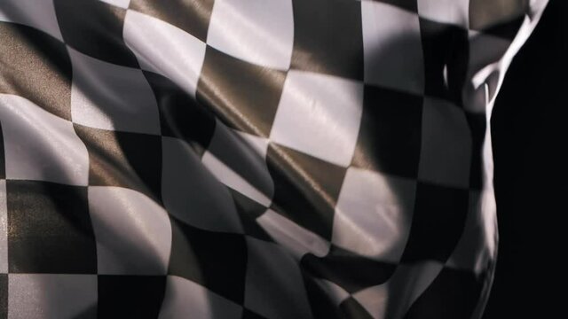 Racing flag silk fabric fluttering wave on black studio background. Checkered flag formula one car motor sport. Official finish start race. Racing flag waving. Slow motion. Close up.