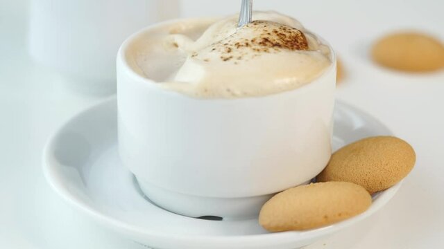 Camera movement on fresh cappuccino coffee with baked cookies. Close up of spoon is stirred with creamy foam and cocoa. Breakfast concept.