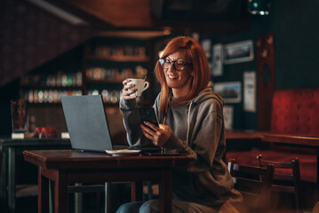 Businesswoman using a laptop and a smartphone while drinking coffee in a cafe