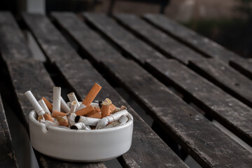 Full ashtray with many cigarette butts put on old dark brown wooden table background. Selective focus and copy space.