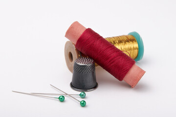 Spools with red and yellow threads, metal thimble and pins with green heads on a white background - obrazy, fototapety, plakaty