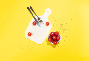 Charry tomatoes in a small bowl on a yellow background with fork and knife. Minimal flat lay.