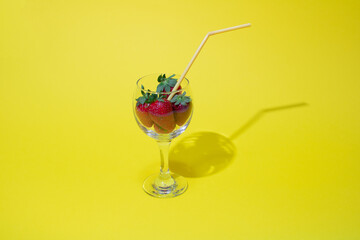 Glass with strawberries and straws on a yellow background.