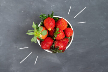 A lot of ripe red strawberries with green leaves in a white plate on the background of a chalk board with strokes of chalk