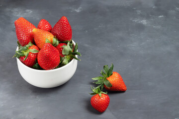 Ripe red strawberries with green leaves in a white plate on a chalk board background