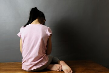 Child abuse concept. The back view of an orphanage girl sitting alone in dark room with her face to...