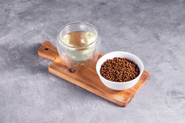 Decaffeinated buckwheat tea in granules in a white plate and brewed in a glass glass on a wooden...