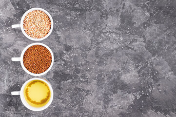 Raw buckwheat, buckwheat tea granules and brewed tea in white cups on a gray background kipi space...