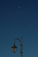 A street lamp with the background of the blue sky and the moon.