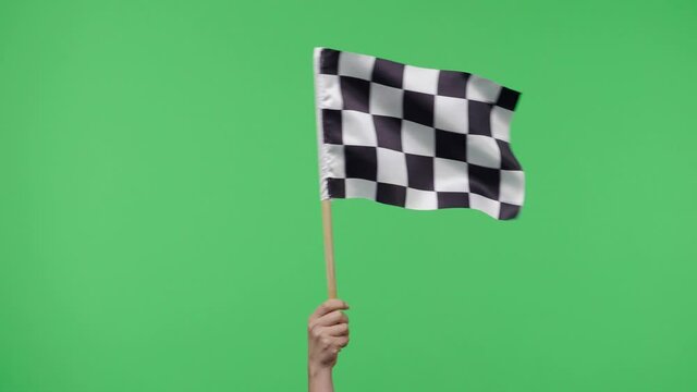 Female hand holding and waving checkered race flag in slow motion against green screen background. Victory, achievement, success, sport concept. Silk black and white checkered flag finish start race.