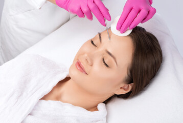 Obraz na płótnie Canvas A procedure for cleansing the skin of the face from blackheads and acne. Cosmetologist treats problematic skin of a young woman's face in a beauty salon. Aesthetic cosmetology and makeup concept.