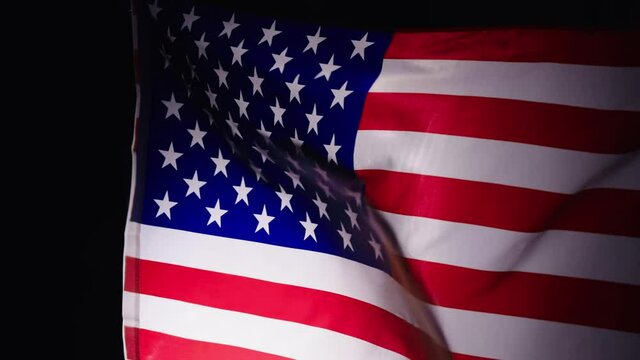 American flag waving on a black studio background. The large flag of the United States of America flutters. Slow motion of the USA flag. National American symbol of freedom and democracy close up.