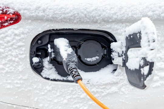 Power supply connect to electric vehicle for charging battery, Charging an electric car in public station by the street in snowing day, Snow covered the car, Green energy, Amsterdam, Netherlands.