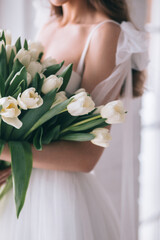 Wedding bouquet of white tulips in the hands of a beautiful bride indoor. Selective Focus