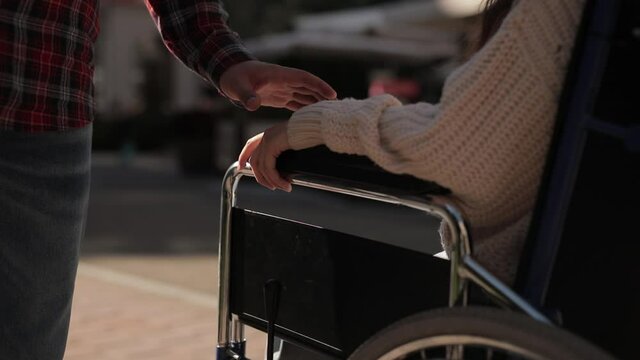 Help and support for disabled invalid people. Man put his hand on hand of disabled woman on wheelchair, close up faceless shot