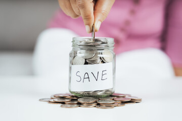 women hand putting money coin into glass jar for saving money. saving money and financial concept