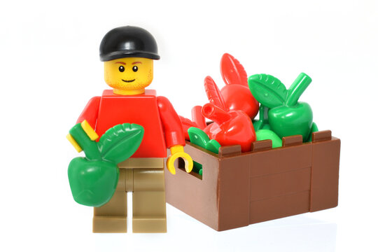 Lego minifigure in red with green apple fruit in hand isolated on white. Editorial illustrative image of fruits harvest.