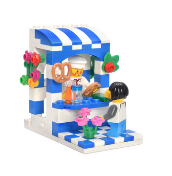 Lego minifigure baker on bakery shop is selling a pretzel to girl isolated on white. Editorial illustrative image of Octoberfest in Bavaria Germany.