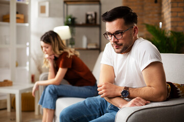 Fototapeta premium Couple at home after having a fight. Sad depressed man sitting on sofa..
