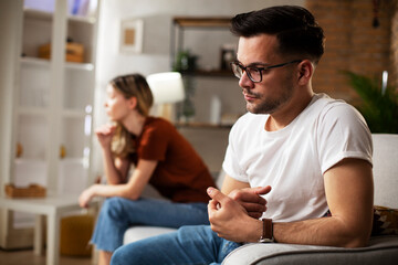 Obraz premium Couple at home after having a fight. Sad depressed man sitting on sofa..