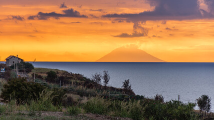 A view of a smoking Stromboli (an island volcano) as seen from the shore of a sleepy town in...