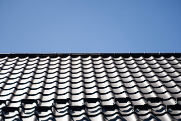 Obraz premium Brown corrugated metal profile roof installed on a modern house. The roof of corrugated sheet. Roofing of metal profile wavy shape. Modern roof made of metal. Metal roofing.