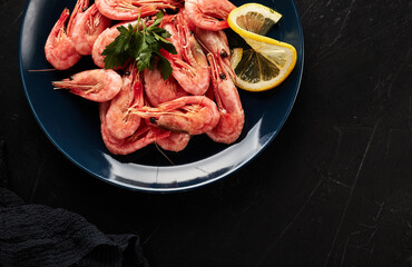 shrimp on a blue plate with lemon on a black textured background top view