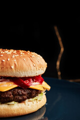 burger on a blue plate on a black background with a golden twig overhead side view