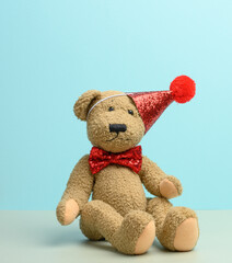 brown teddy bear in a red cap sits on a blue background,