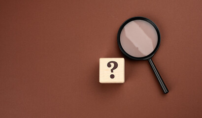 black magnifier on a brown background and question marks. The concept of uncertainty and the search...