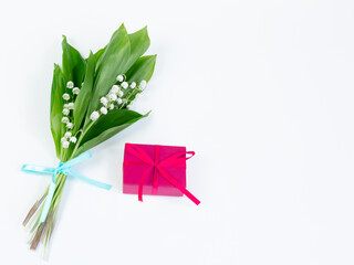 Fototapeta Bukiet kwitnących konwalii majowych , przewiązanych błękitną wstążką, i różowe pudełko prezent, przewiązane kokardką, na białym tle obraz