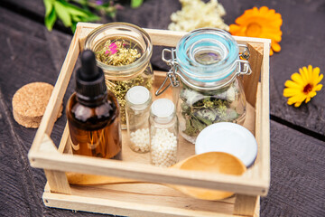 Homeopathic medicine pills on wood table, globules in jars and in wood box decorated with various herbal medicinal plants outdoors in summer, wooden background. Homeopathy concept.