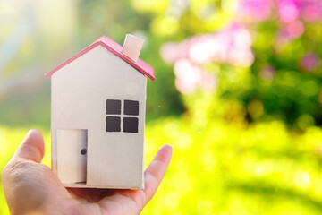 Miniature model house in female woman hand on green outdoor background. Eco Village, abstract environmental background. Real estate mortgage property insurance dream home ecology concept.