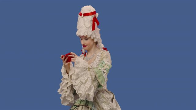 Portrait of courtier lady in white vintage lace dress and wig plays game on smartphone and wins. Young woman posing in studio with blue screen background. Close up. Slow motion ready 59.94fps.