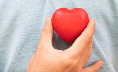 hand holding a red heart to his chest.Health, medicine, cardiology concept.Heart health insurance, organ donation concept.World mental health day.World heart health day.heart selective focus.