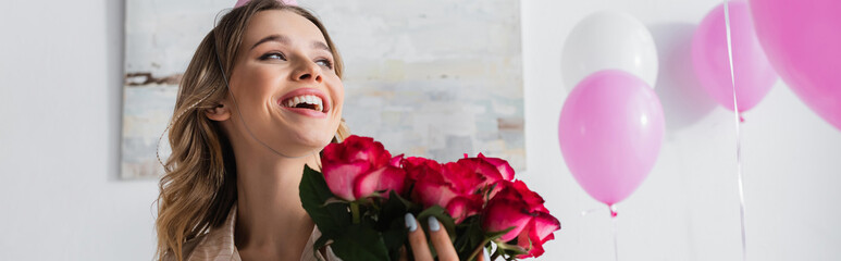 Happy woman holding roses near balloons at home, banner