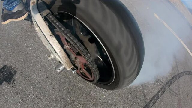 Motorcycle trick tire burnout closeup, tire rubbing against asphalt. Slow motion