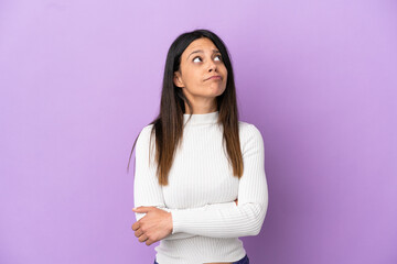 Obraz premium Young caucasian woman isolated on purple background and looking up