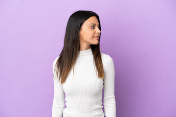 Young caucasian woman isolated on purple background looking to the side