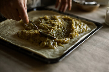 Male hands spreading onion pie filling on a baking sheet