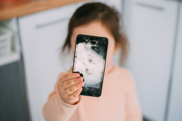 Broken glass smartphone screen in the hand of a frustrated girl, at home in the kitchen