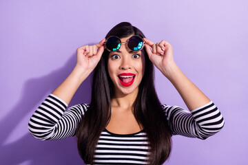 Photo of pretty shocked young lady wear striped shirt arms dark eyewear smiling isolated purple color background