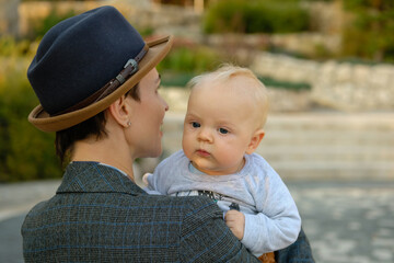 Beautiful business woman in suit and hat holds baby in her arms.