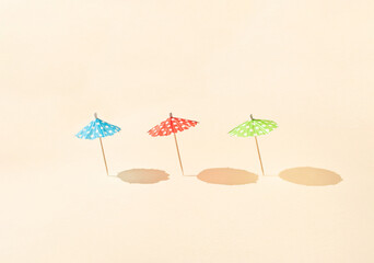 Colorful sun umbrellas with sunny day shadows against bright beige background. Minimal summer vacation concept. Creative beach idea.