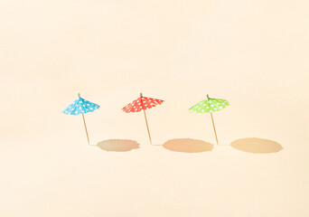 Obraz premium Colorful sun umbrellas with sunny day shadows against bright beige background. Minimal summer vacation concept. Creative beach idea.