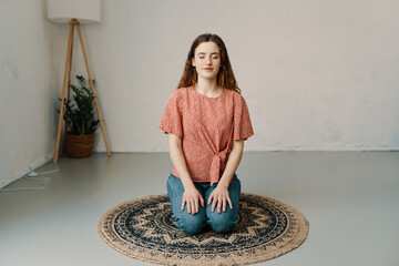 Young woman kneeling on a round mat at home meditating